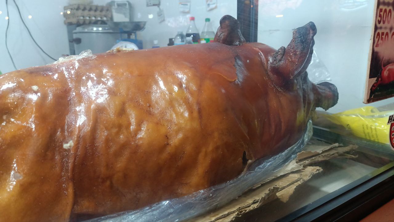 A whole lechon in a vendor's display case at Sugbo Mercado, Cebu, with a handwritten price board beside it