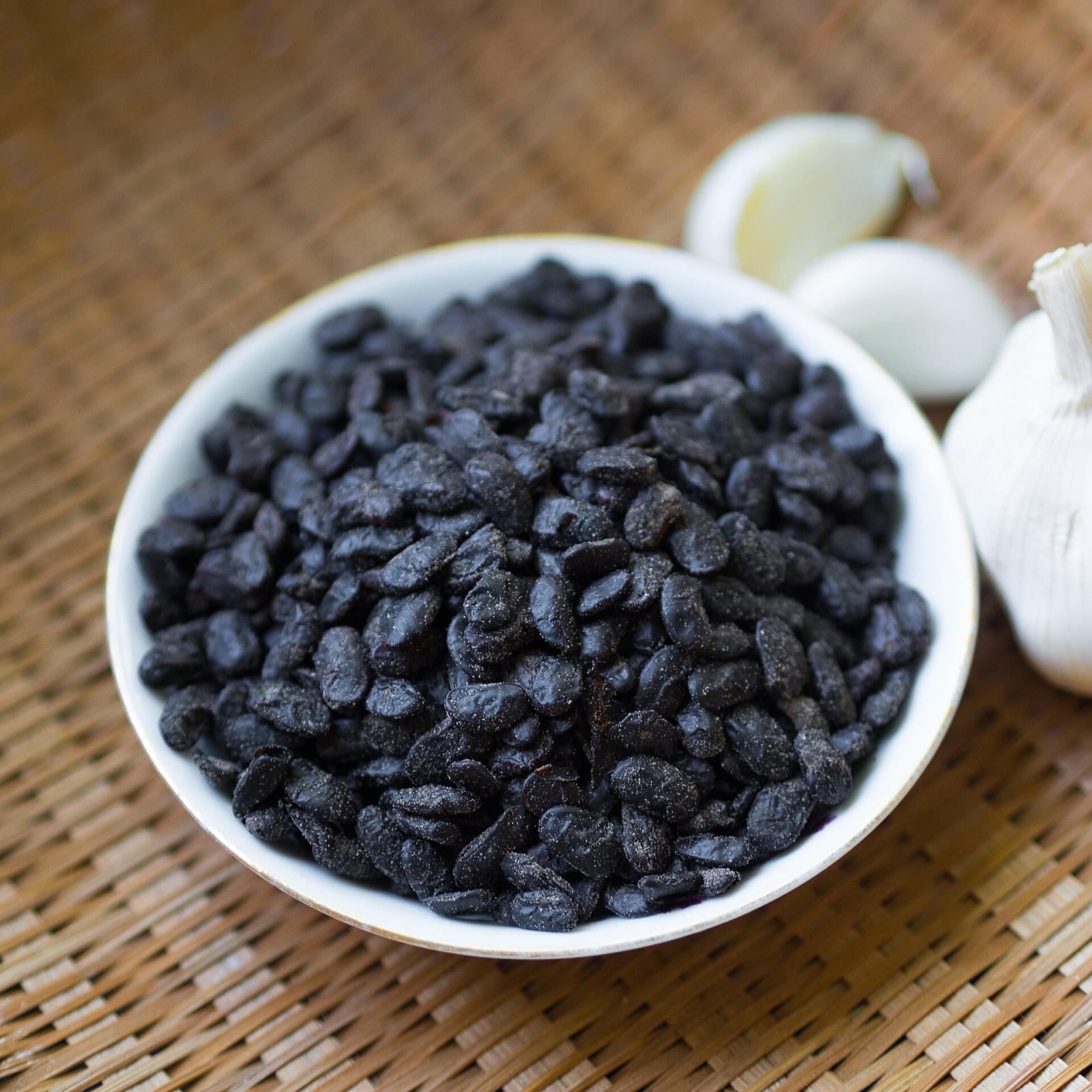 A small bowl of dried fermented black beans, with garlic cloves beside it for scale